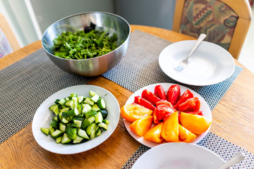 Wooden table with setting of healthy vegan lunch or dinner and green vegetables, arugula salad, cucumbers sliced cut tomatoes in home apartment house in summer