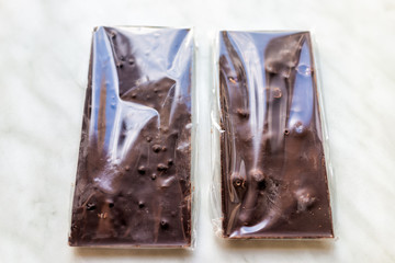 Flat top closeup of two packaged in plastic milk or dark chocolate bars with fruits and nuts hazelnuts almonds on table