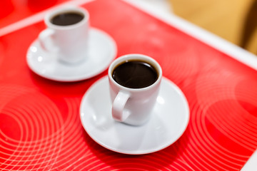 Closeup of two espresso shots dark roast coffee cups with detail and texture of black brown liquid on plate and red background table in Italy cafe breakfast