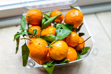 Closeup Of Plastic Box With Many Satsuma Mandarin Oranges On Floor With Vibrant Vivid Color And Green Leaves Fruit