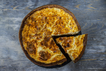 Wall Mural - Traditional French Quiche Lorraine pie with a slice cut, seen from above, on display on a rustic wooden table. It is an iconic dish of Eastern France, a pastry made of flan, cheese, cream & ham