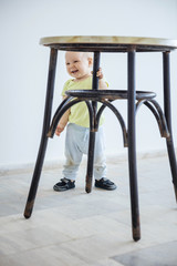 Wall Mural - Cute baby girl standing while gripping leg of stool and laughing