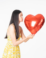 Wall Mural - Asian young woman in yellow dress hold  red balloon heart. Young woman holding it with  being excited and surprised  holiday present isolated white  background.concept love surprise valentine day.