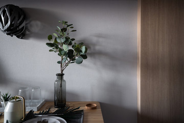 Close up cozy dining table corner in scandinavian / nordic style with ceramic plate setting on napery with candle and artificial plants and gold utensils / Cozy interior concept / setting scene