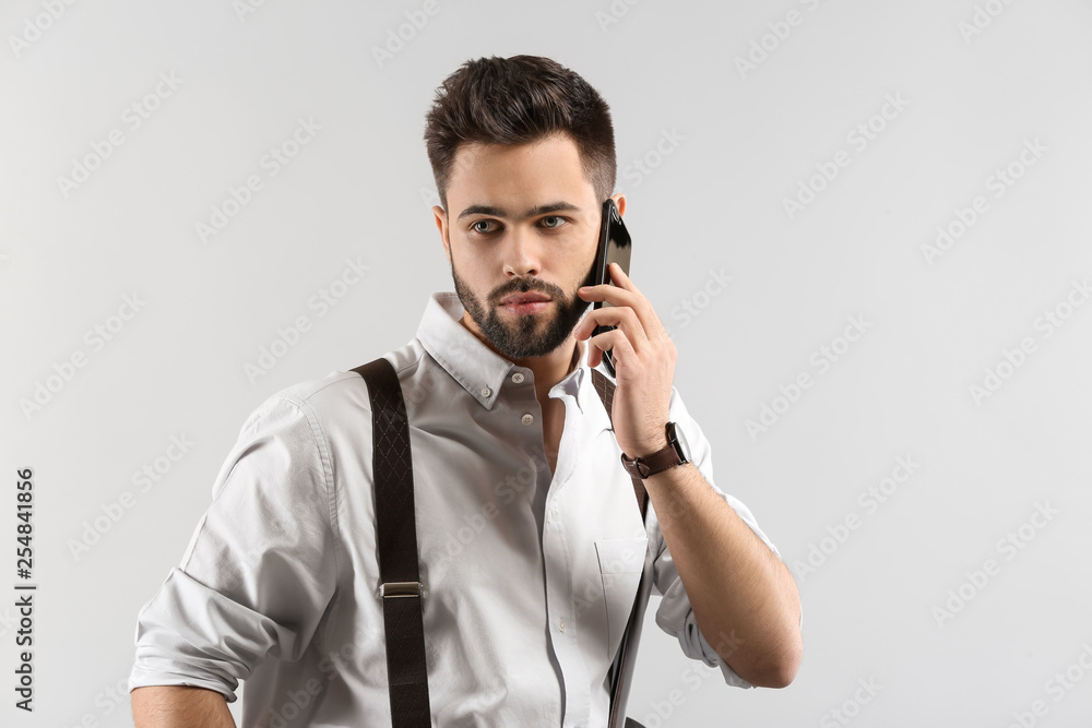 Fashionable young man talking by phone on light background
