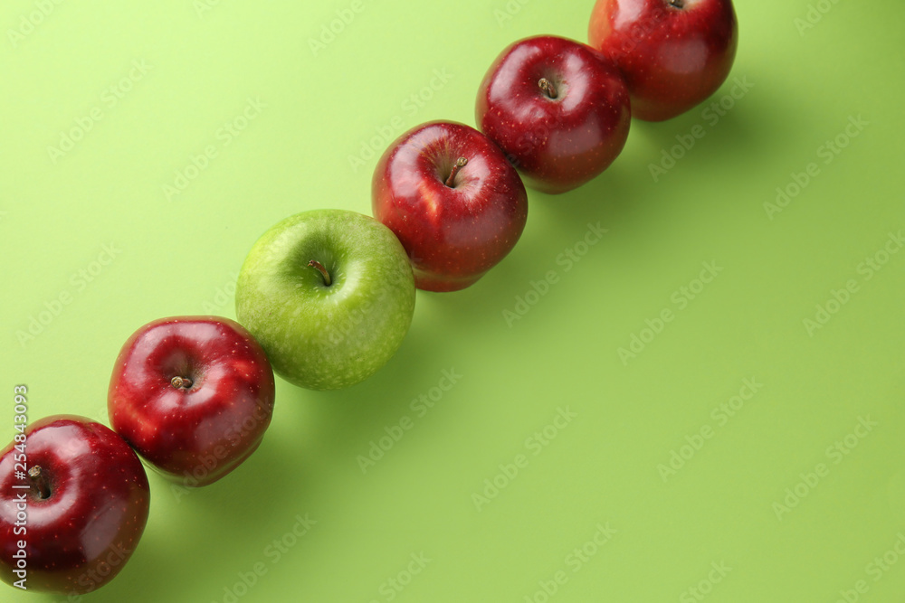 Green apple among red ones on color background. Concept of uniqueness