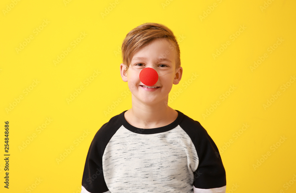 Funny little boy with clown nose on color background. April fools' day celebration