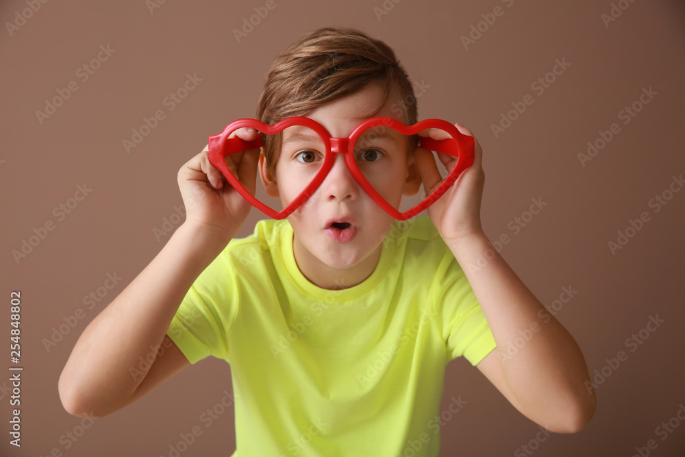 Funny little boy with big glasses on color background