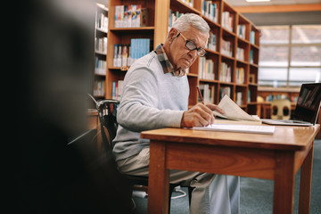 Wall Mural - Senior man writing sitting in a university classroom