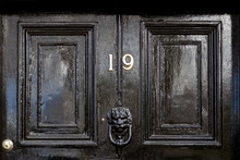 House Number 19 In Bronze On A Black Wooden Entrance Door With The Nineteen In Bronze Numerals And A Black Lions Head Door Knocker