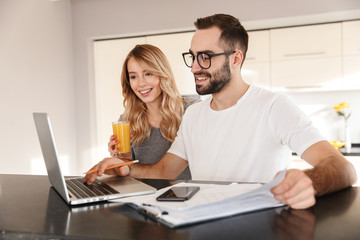 Wall Mural - Amazing happy young loving couple sitting at the kitchen using laptop computer.