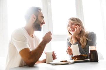 Sticker - Young loving couple sitting at the kitchen have a breakfast talking with each other.