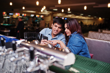 Stylish asian couple wear on jeans sitting on chair at bar in club and look on phone.