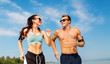© Syda Productions - fitness, sport and technology concept - happy couple with earphones and arm bands running along summer beach