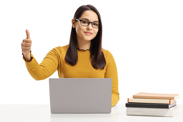 Wall Mural - Young female sitting at a table with laptop and books showing thumbs up