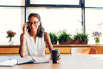 Wall Mural - Smiling female entrepreneur talking on smartphone in cafe