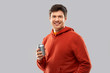 drinks and people concept - happy young man in red hoodie drinking soda from tin can over grey background