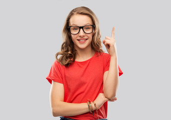 Poster - education, school and people concept - smiling teenage student girl in glasses and red t-shirt pointing finger up over grey background