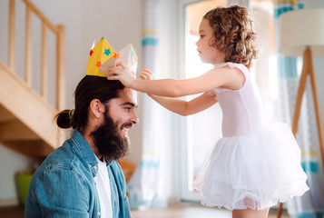 Wall Mural - A small girl putting a paper crown on father's head at home when playing.