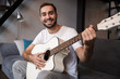 © Drobot Dean - Photo of european man playing acoustic guitar while sitting on sofa in apartment
