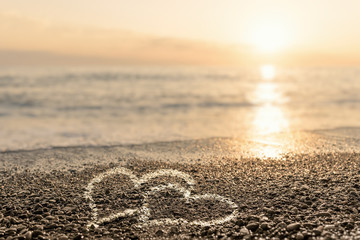 Two hearts painted on the beach at sunset. The concept of romance and love.