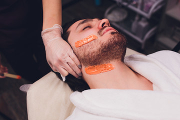 Hair removal. Man's face sugaring epilations beard trimming, yellow color, in cosmetology on the couch.