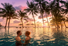 Couple At Beach Vacation Holidays Resort Relaxing In Swimming Pool With Scenic Tropical Landscape At Sunset, Romantic Summer Honeymoon Island Destination, Coconut Palm Tree Near The Sea