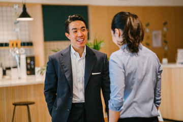 A Chinese Asian business man professional is having a casual discussion with a Chinese Asian woman in the office cafe during the day. Image taken with a blur foreground and  background.