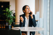 © Danon - An elegant Indian woman sitting inside a cafeteria. She is smiling while talking to a friend over the phone.