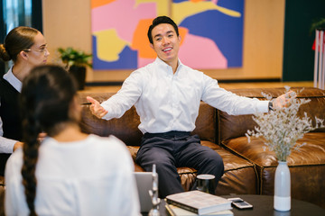 Wall Mural - A youthful Asian Chinese expert is giving an introduction before his partners in the workplace. He is wearing a white polo shirt and dark jeans.
