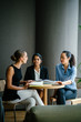 © Danon - A young Caucasian woman is having a casual business meeting with her team in a meeting room. They are sitting and having an animated conversation. The team is diverse (Indian and Chinese).
