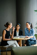 © Danon - A young Caucasian woman is having a casual business meeting with her team in a meeting room. They are sitting and having an animated conversation. The team is diverse (Indian and Chinese).