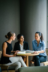 A young Caucasian woman is having a casual business meeting with her team in a meeting room. They are sitting and having an animated conversation. The team is diverse (Indian and Chinese). 