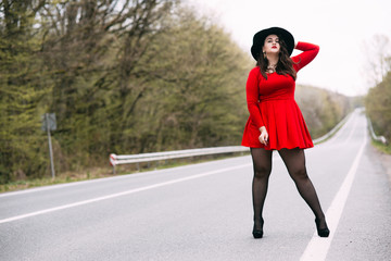 Young stylish woman wearing red dress, black hat walking on the city street in autumn. Fall fashion, elegant look. Plus size model.