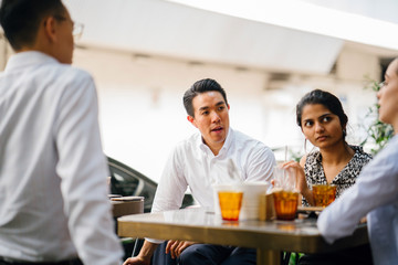 A diverse team of business people is having a productive and efficient meeting. They are sitting around each other at a table and having an animated discussion.