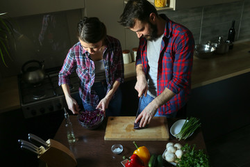 Beautiful young couple in kitchen at home while cooking healthy food. Husband cut cabbage. Wife mix salad. Scene from family life.