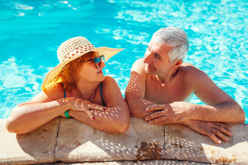 Wall Mural - Senior couple relaxing in swimming pool. People enjoying summer vacation. All inclusive.