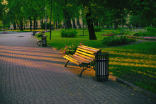 A Wooden Bench In A Summer Park Is Beautifully Lit By The Setting Sun.