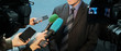 © romsvetnik - Interview, report, media. Abstract man in a suit and tie speaks to reporters and video cameras. Female hands hold microphones, voice recorders and mobile phones to record sound.