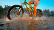 LOW ANGLE: Unrecognizable mountain biker rides past camera in the river shallows
