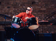 © Fxquadro - Young stylish musician in sunglasses sits behind the drum set against a brick wall, perform in night club