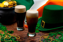 St Patricks Day Party And Irish Celebration Of Patron Saint Concept Theme With Frothy Glasses Of Dry Stout, Green Hat With A Buckle, A Pot Of Gold, The Flag Of Ireland And Beads With Shamrock In A Pub