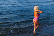 lady in boater and pink swimsuit walk on ocean shore. back to ca