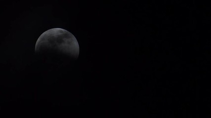 Wall Mural - thin clouds slowly reveal a full moon during a lunar eclipse. moon on left side of frame.