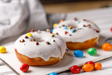 Cookery, baking and food concept - closeup. Two donuts in white glaze with color chocolate dragee on a decorative board on a dark background.