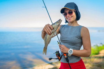 Wall Mural - Happy fisher girl with walleye zander fish trophy at lake shore