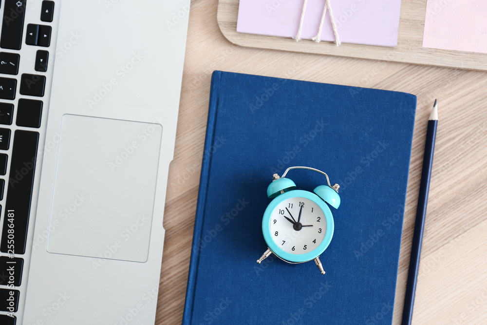 Notebook, alarm clock and laptop on wooden table