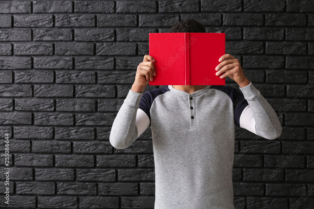 African-American schoolboy with book on dark background