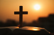 Silhouette of the wooden cross over opened bible with a bright sunrise as background , Christian, god.