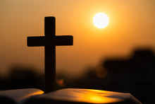 Silhouette Of The Wooden Cross Over Opened Bible With A Bright Sunrise As Background , Christian, God.